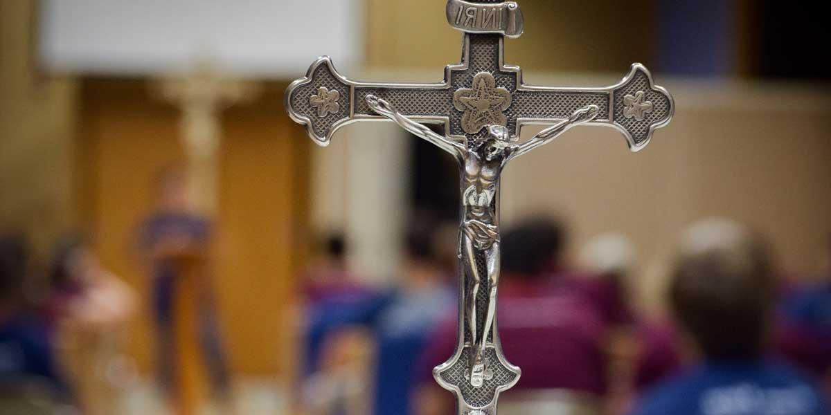 A silver crucifix with a speaker and audience out of focus in the background